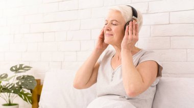 Mutlu son sınıf öğrencisi bir koltukta oturmuş kulaklıkla müzik dinliyor. Rahatlamış ve odaklanmış görünüyor, müzik çalmaktan hoşlanıyor..