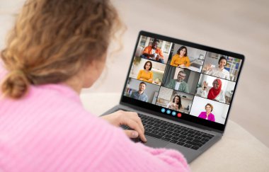 Bir kadın masada oturuyor ve dizüstü bilgisayara bakıyor. Diğer sekiz kişiyle birlikte bir video konferans görüşmesine katılıyor. Ekrandaki insanlar bir ızgara düzeninde