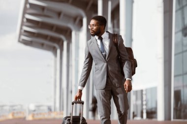 Modern bir havaalanının önünde bavulla yürüyen siyah işadamı iş gezisine ya da seyahate çıkmaya hazır..