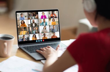 Kırmızı tişörtlü bir kadın bilgisayarındaki büyük bir video konferansına katılıyor. Elleri koşu pistinde ve odaklanmış bir ifadeyle ekrana bakıyor..