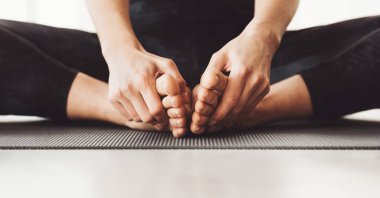 Eğri büğrü bacaklı bir yoga minderinde oturan kadın ayak parmaklarını yavaşça öne çekiyor.