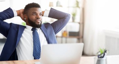 Takım elbiseli bir işadamı masasında ellerini başının arkasına koyup işine ara veriyor..