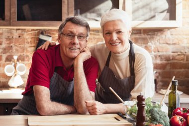 Önlük takan son sınıf bir çift mutfaklarında birlikte yemek pişiriyor, birbirlerine gülümsüyor ve görünüşe göre birlikte vakit geçiriyorlar. Malzemeler ve aletler tezgahta görünür.