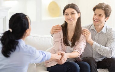 Genç bir çift sıcak, güneşli bir oturma odasında danışman ile konuşurken sıcak bir şekilde gülümsüyor. Danışman dikkatlice dinliyor ve çiftle yakınlaşıyor, el sıkışıyor.