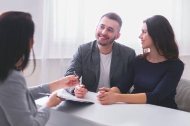 Mutlu çift, mali danışmanın karşısında oturuyor. Kadın gülümsüyor ve adam ona bakarken, danışmana bakıyor. Danışman masadaki bir belgeyi işaret ediyor.