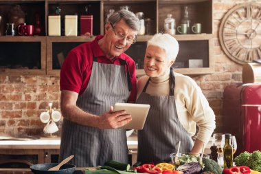 Mutfaklarında önlük takan bir çift tarif bulmak için tablet kullanıyorlar. Taze sebzeleri ve salataları hazır..