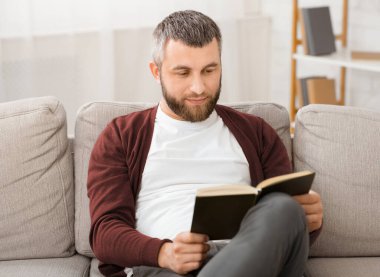 Sakallı adam bir kanepede rahatça oturur, okuduğu bir kitaba dalmıştır. Oda, sayfaları çevirirken sessizdi. Sadece önündeki kelimelere odaklanırdı..