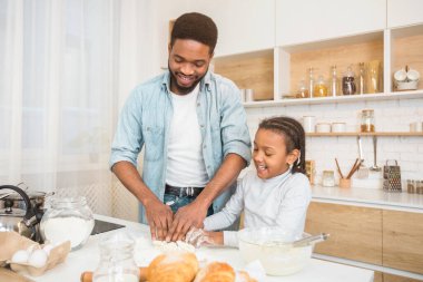Mutlu Afro-Amerikan baba ve kızı ev mutfağında hamur yoğuruyor.