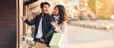 Bir adam ve bir kadın ellerinde alışveriş torbalarıyla şehir caddesinde dikiliyorlar..