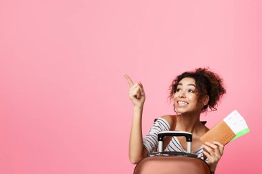 Kıvırcık saçlı neşeli bir Afrikalı Amerikalı kadın elinde pasaport ve biniş kartı tutarken yaklaşan seyahati için heyecanlı görünüyor.