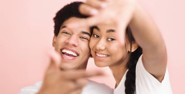 Neşeli, genç bir Afro-Amerikan çift gülümseyip neşeli pembe bir arka planla poz veriyor. İkisi de beyaz gömlek giyiyor ve heyecanlı ve mutlu görünüyorlar. Birlikte neşeli bir anı paylaşıyorlar..