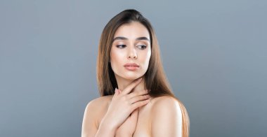 Düz, uzun kahverengi saçlı genç bir kadın gündüz vakti iyi ışıklandırılmış bir stüdyoda gri bir arka planda eli göğsünde poz veriyor. Düşünceli ve sakin görünüyor.