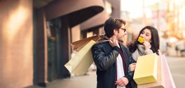 A man and woman are standing on a busy street, holding shopping bags. clipart