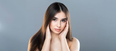 Uzun kahverengi saçlı ve açık tenli genç bir kadın ellerini yüzünü gri bir arka plana yaslayarak poz veriyor. Sakin ve sakin bir ifade yayıyor, web pankartı gibi.