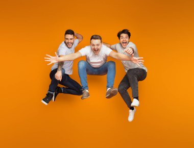 Heyecanlı arkadaşlar turuncu stüdyo arka plan üzerinde birlikte atlama