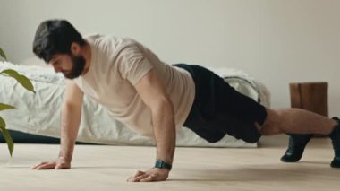 Güç egzersizi. Genç sakallı adam şınav çekiyor, evde egzersiz yapıyor, yandan bakıyor.