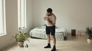 Esneme egzersizi. Genç sakallı adam evde antrenman yapıyor, kalçasını çeviriyor.