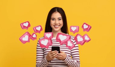 Hoş, neşeli, genç Asyalı bir kadın. Günlük kıyafetler giyiyor, cep telefonu tutuyor, erkek arkadaşına mesaj atıyor, cep telefonu uygulaması kullanıyor, sarı stüdyo geçmişi var.