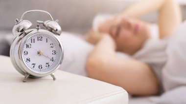 Dijital ekranlı bir çalar saat, temiz beyaz bir masanın üzerinde, iyi ışıklandırılmış bir odada bir gölge oluşturur. Saat numaraları, son sınıftaki bayanın uyuduğu zamanı gösteriyor.