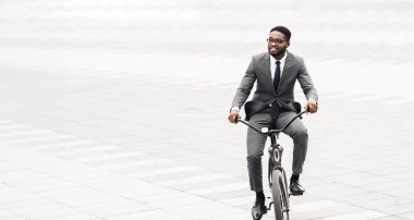 Siyahi profesyonel, modern bir şehir üzerinden ofise bisikletle gidiyor. Atmosfer canlı ve kentsel, işe bisikletle gitmenin verimliliğini ve çevre dostluğunu vurguluyor..