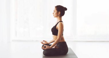 Siyah bluz giyen bir kadın dışarıda yoga pozu veriyor. Odaklanmış ve dengeli, esnekliği ve gücü arttırmak için çeşitli gerilmeler ve hareketler yapıyor.