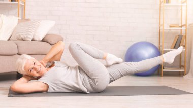 Son sınıf öğrencisi kadın yere serilmiş bir minder üzerinde yoga pozu veriyor. Odaklanmış ve konsantre görünüyor. Vücut hareketlerinde esneklik ve güç gösteriyor..