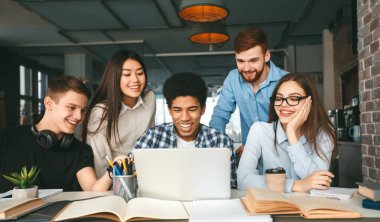 Üniversite öğrencileri kütüphanede birlikte okuyorlar, birlikte dizüstü bilgisayar kullanıyorlar.