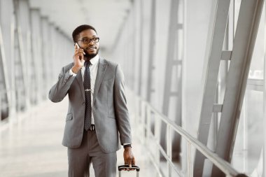 Modern bir havaalanının önünde elinde bavuluyla Afro-Amerikalı bir işadamı telefonuyla bekliyor. Çevre profesyoneldir ve hareketlidir, yoğun bir seyahat gününü yansıtır..