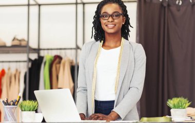 Coşkulu bir Afrikalı Amerikalı kadın moda tasarımcısı stüdyosunda ölçüm bandıyla poz veriyor.