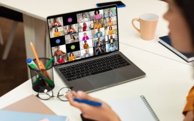 Bir dizüstü bilgisayar ekranı, çeşitli geçmiş ve etnik kökenlere sahip birden fazla katılımcının yer aldığı bir video konferans görüşmesini görüntüler, hepsi ayrı video karelerinde görünür.