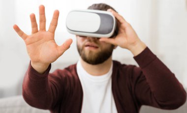 Sakallı bir adam sanal gerçeklik kulaklığı takıyor ve kendisini dijital ortama daldırıyor. Sanal dünyayla etkileşime girerken yüz hatları cihaz tarafından kısmen gizleniyor.