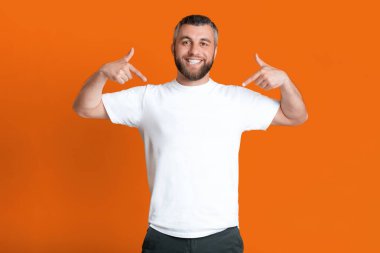 Beyaz gömlekli ve siyah pantolonlu bir adam sıradan bir poz veriyor ve önüne bakıyor. Kıyafet seçiminde rahat ve kendinden emin görünüyor..