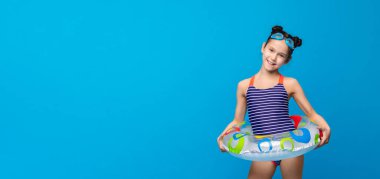 Yaz tatilinin tadını çıkarıyorum. Şişme halka ve yüzme gözlüğü, mavi stüdyo arka plan ile poz mayo Sevimli küçük kız