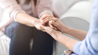 Bir kadın, sıcak bir oturma odasında samimi bir konuşma sırasında başka bir kadının elini tutarak rahatlık ve güven veriyor.