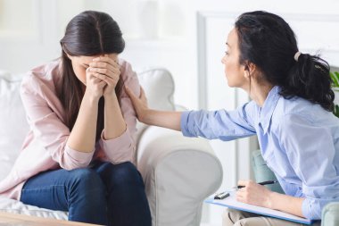 Ağlayan kadın bir kanepede oturuyor ve bir terapistle konuşuyor. Her iki şahıs da özenli ve tartışmalara odaklanmış görünüyor..