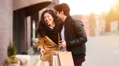 Bir adam ve bir kadın bir binanın önünde ellerinde alışveriş torbalarıyla duruyorlar..