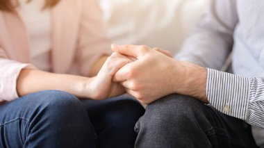Bir adam ve bir kadın koltuğa oturmuş, el ele tutuşuyorlar. Birbirlerine karşı sevgi ve bağlılık ifadeleriyle bakıyorlar. Oturma odası ayarları rahat ve samimi bir atmosfer olduğunu gösteriyor.