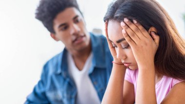 Mavi kot gömlek giyen Afro-Amerikalı genç adam endişeli genç bir kıza bakıyor. Kız ellerini yüzünü kapatarak oturuyor, üzüntüsünü ve üzüntüsünü ifade ediyor..