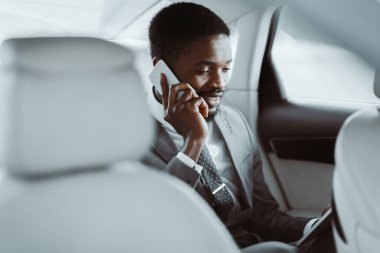 Takım elbiseli ve kravatlı Afro-Amerikalı bir işadamı bir arabanın arka koltuğunda oturur. Akıllı telefonuyla konuşuyor ve bir iş görüşmesinin ortasındaymış gibi görünüyor..