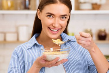 Genç bir kadın mutfaktaki kaseden mısır gevreği yerken gülümsüyor..