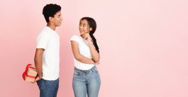 Genç bir Afrikalı Amerikalı, pembe arka planlı parlak ışıklı bir odada ortağına hediyeyle sürpriz yapıyor. Her ikisi de sıradan giyinmiş ve gülümsüyor, mutlu bir anı yakalıyorlar, boşluğu kopyalıyorlar.