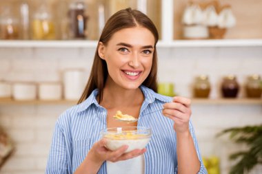 Bir kadın mutfakta mısır gevreği yerken gülümsüyor..