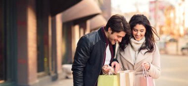 Genç çift alışverişlerini kontrol ediyor, butik alışverişinden sonra alışveriş çantalarına bakıyor.