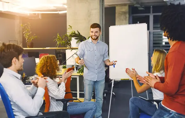 stock image A man stands in front of a group of attentive individuals, gesturing and speaking confidently as he delivers a presentation. The audience is seated, listening intently, taking notes