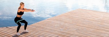 Spor Giyim Antrenmanında Güzel bir kadın dışarıda direniş çemberiyle egzersiz yapıyor, Ortaçağ bayan antrenmanı yapıyor, tahta iskele kıyısında, göl kenarında, gülümseyen kadın dışarıda çalışmaktan hoşlanıyor, kopyalama alanı kullanıyor.