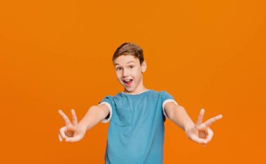 İki zafer işaretleri veya barış hareketleri, turuncu studio arka planda gösterilen mutlu duygusal öğrenci