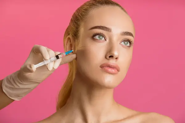 stock image A close-up photo of a woman receiving a facial injection treatment. The woman is looking up and has a serious expression. The injection is being administered by a gloved hand