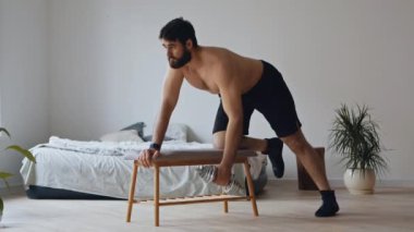Güçlü kaslı bir adam evde dambıl eğitiyor.