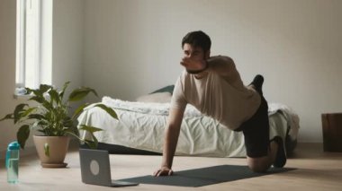 Fitness devrede. Sakallı adam evde laptopla paspas üstünde egzersiz yapıyor.