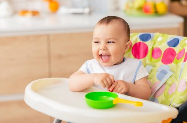 Sevimli bir erkek bebek mutfakta çocuk sandalyesinde oturuyor. Sahne parlak ve neşeli, evdeki bir çocuğun masumiyetine ve mutluluğuna odaklanmış..